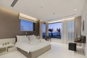 Een moderne hotelkamer met een groot bed, een nachtkastje, een klein tafeltje en uitzicht op de oceaan.