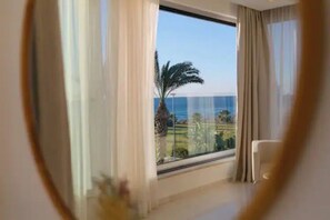 Ein Zimmer mit großem Fenster, Meerblick und einer Palme davor.