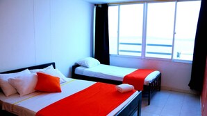 Une chambre d’hôtel avec deux lits, chacun agrémenté de linge de lit blanc et de touches de couleur orange, une grande fenêtre offrant une belle vue et un sol carrelé.