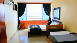 A hotel room with two beds, a small table, a TV, and a window with curtains.