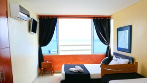 A hotel room with two beds, a small table, a TV, and a window with curtains.