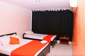 Una habitación con dos camas, cada una con una colcha blanca y naranja, una mesita de noche de madera y una cortina negra.