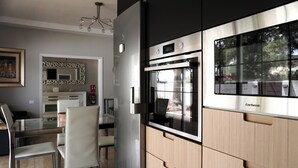 Cozinha moderna com forno de aço inoxidável, mesa de jantar de vidro e armários de madeira clara.