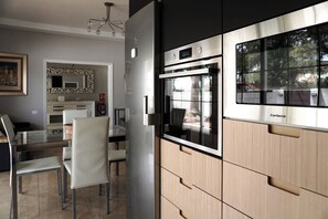 Een moderne keuken met een oven van roestvrij staal, een glazen eettafel en licht houten kasten.