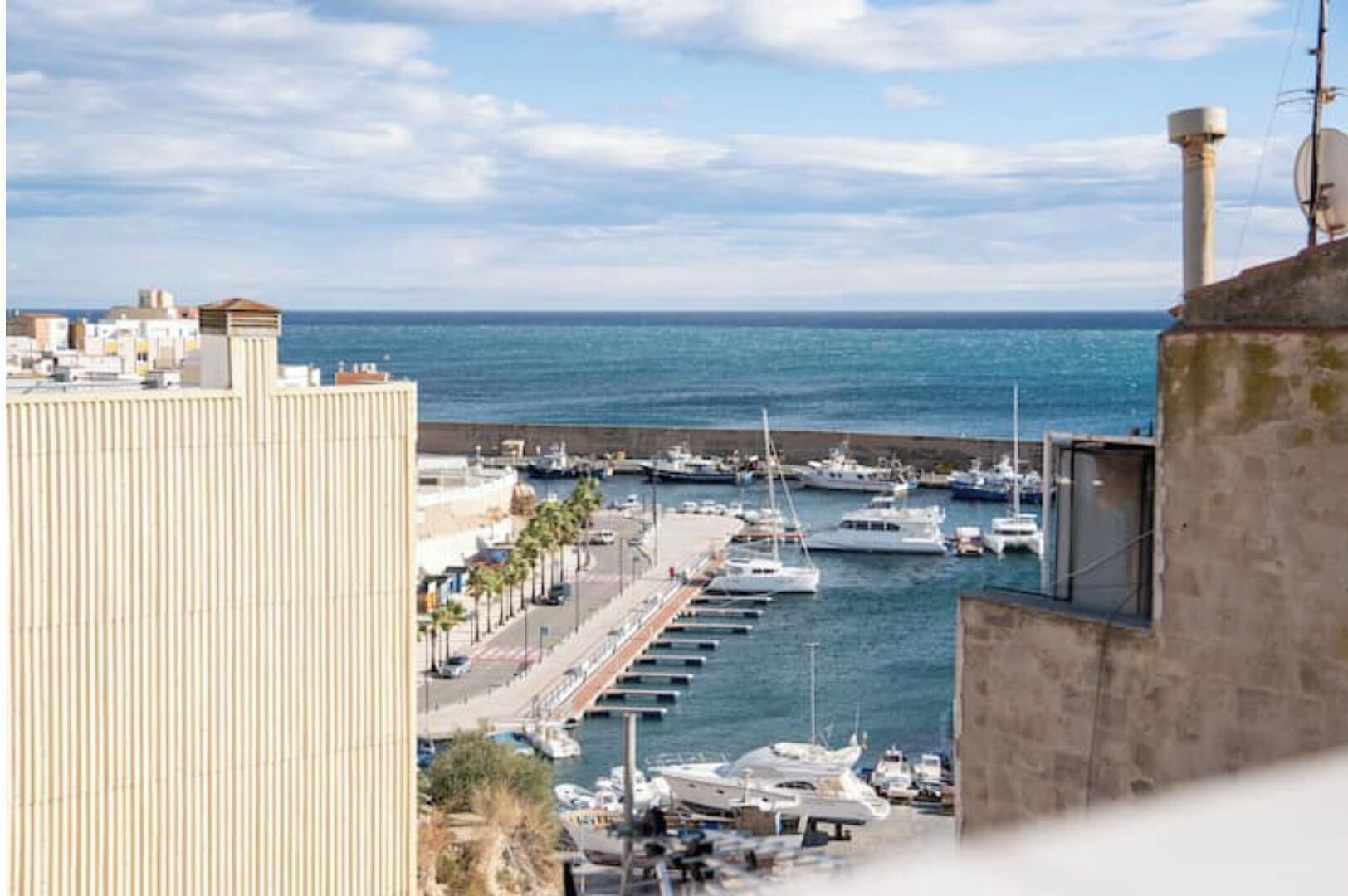 A marina with boats docked, a waterfront promenade, and buildings in the background.