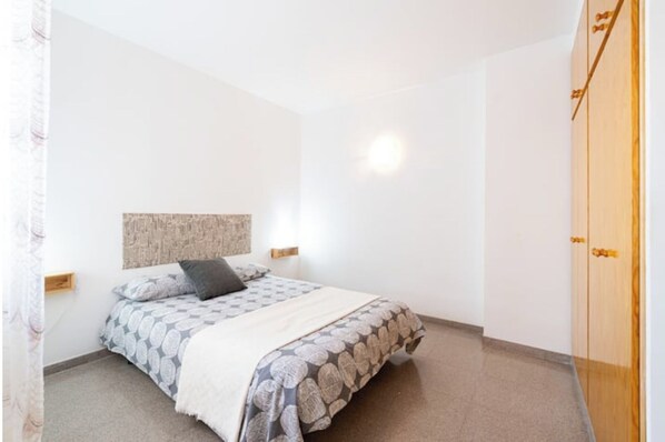 Un dormitorio con cama, cabecera, mesita de noche, armario y luz empotrada en la pared.
