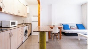 Une cuisine compacte équipée d’un four à micro-ondes, d’un lave-linge et d’une petite table à manger avec des chaises.