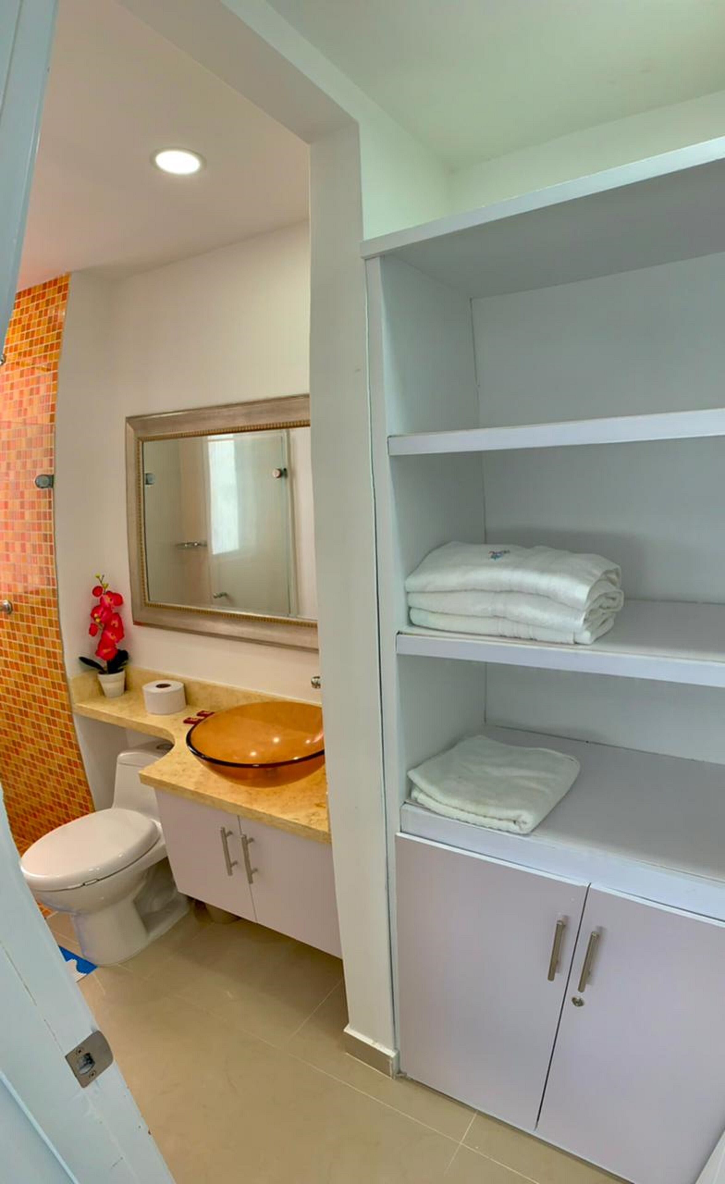Une salle de bain avec un lavabo blanc, un miroir et des étagères où sont pliées des serviettes.