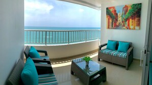 A balcony with a view of the ocean, wicker furniture, and a painting on the wall. - Apartment Al-2 Facing the sea With Wifi (Cartagena)