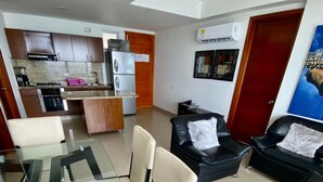 A modern living room with a glass dining table, black leather sofas, and a kitchen in the background. - Apartamento Al-4 Frente al mar Piscina y Wifi (Cartagena)
