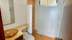 A bathroom with a white toilet, a sink with a brown bowl, a mirror, and a shower with a tiled wall. - Apartamento Al-4 Frente al mar Piscina y Wifi (Cartagena)