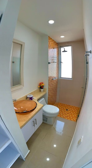 A bathroom with a round sink, toilet, and shower.