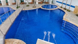 A large indoor swimming pool with a surrounding patio area, including seating and palm trees. - Apartment Al-1 Facing the sea With Pool and Wifi (Cartagena)