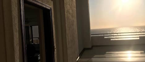 A corridor leading to a balcony with a view of the sea at sunset.