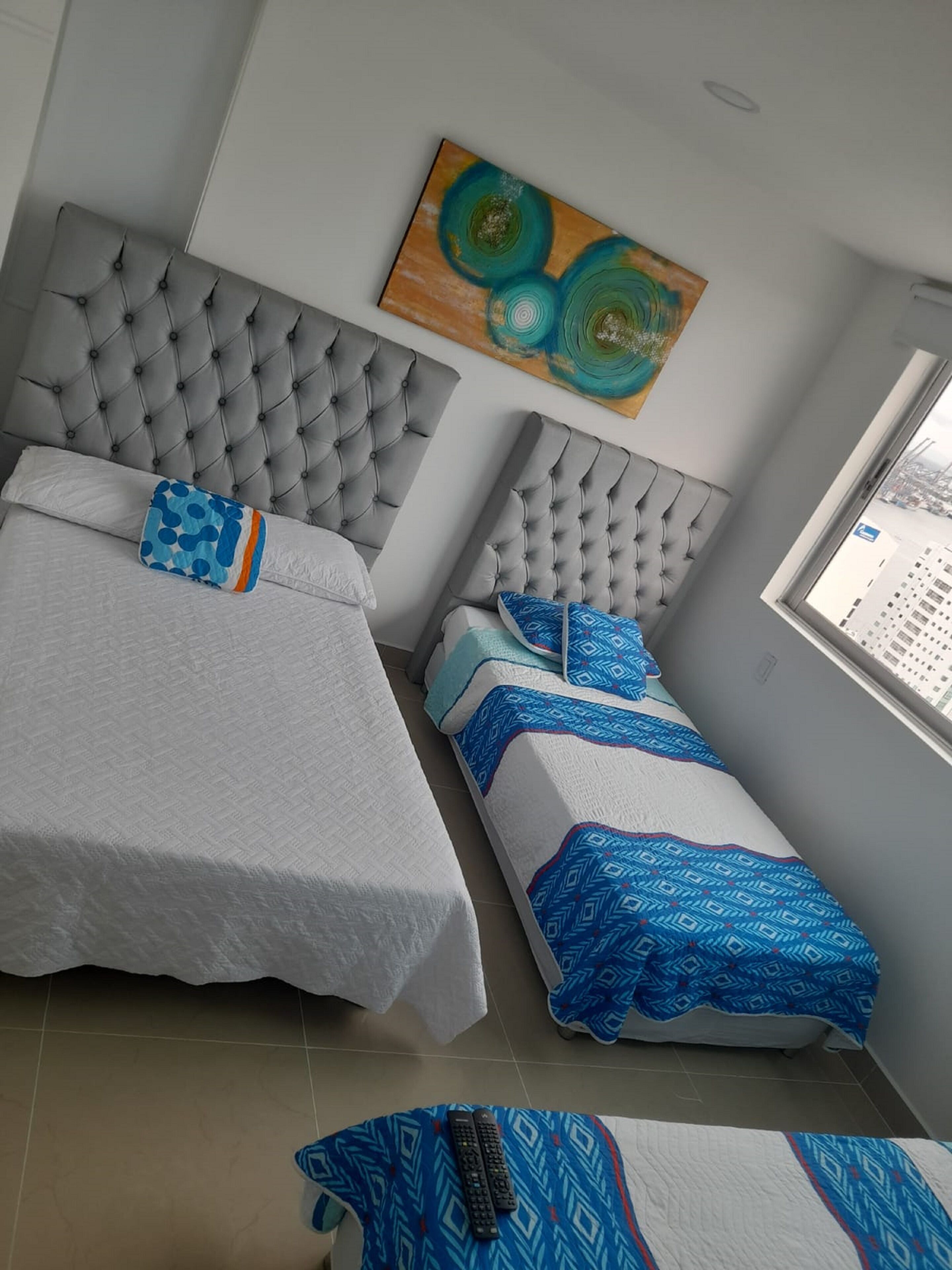 Een kamer met twee bedden, elk met een gestoffeerd hoofdeinde, en een raam met uitzicht op gebouwen.