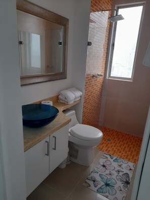 Un baño con inodoro, lavabo, espejo, ducha y ventana.