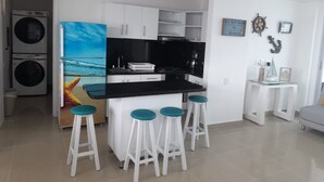 A modern kitchen with white cabinets, a black countertop, and four bar stools with teal seats.