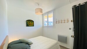 Et soveværelse med en enkelt seng, en pendel, et vindue med gardiner, en radiator og et vægmonteret knagered.