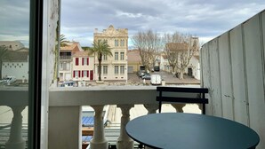 A balcony with a table and chairs, overlooking a street with buildings and a palm tree.