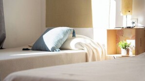 A hotel room with two beds, a bedside table with a lamp, and a small potted plant.