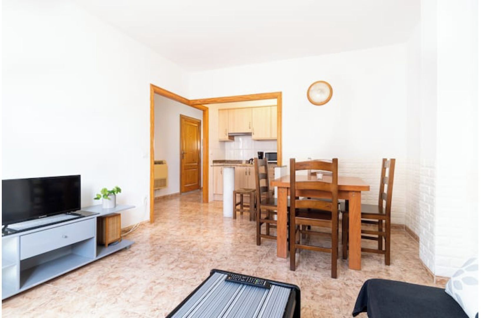 A compact living space with a TV, a small dining table with chairs, a kitchen area, and a sofa.