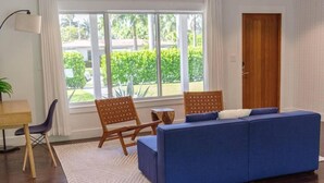 Ein Zimmer mit einem blauen Sofa, Holzstühlen, einem kleinen Tisch und einem großen Fenster mit Blick auf Grünflächen.