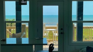 A room with a view of the ocean, a door, a chair, and a small table. - Breezy Ocean View/Sleeps 10/Steps To Beach/Central (Bolivar Peninsula)