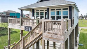 A wooden decked structure with a staircase, a covered area with windows, and a sign that reads 'BREEZY ON THE.' - Breezy Ocean View/Sleeps 10/Steps To Beach/Central (Bolivar Peninsula)