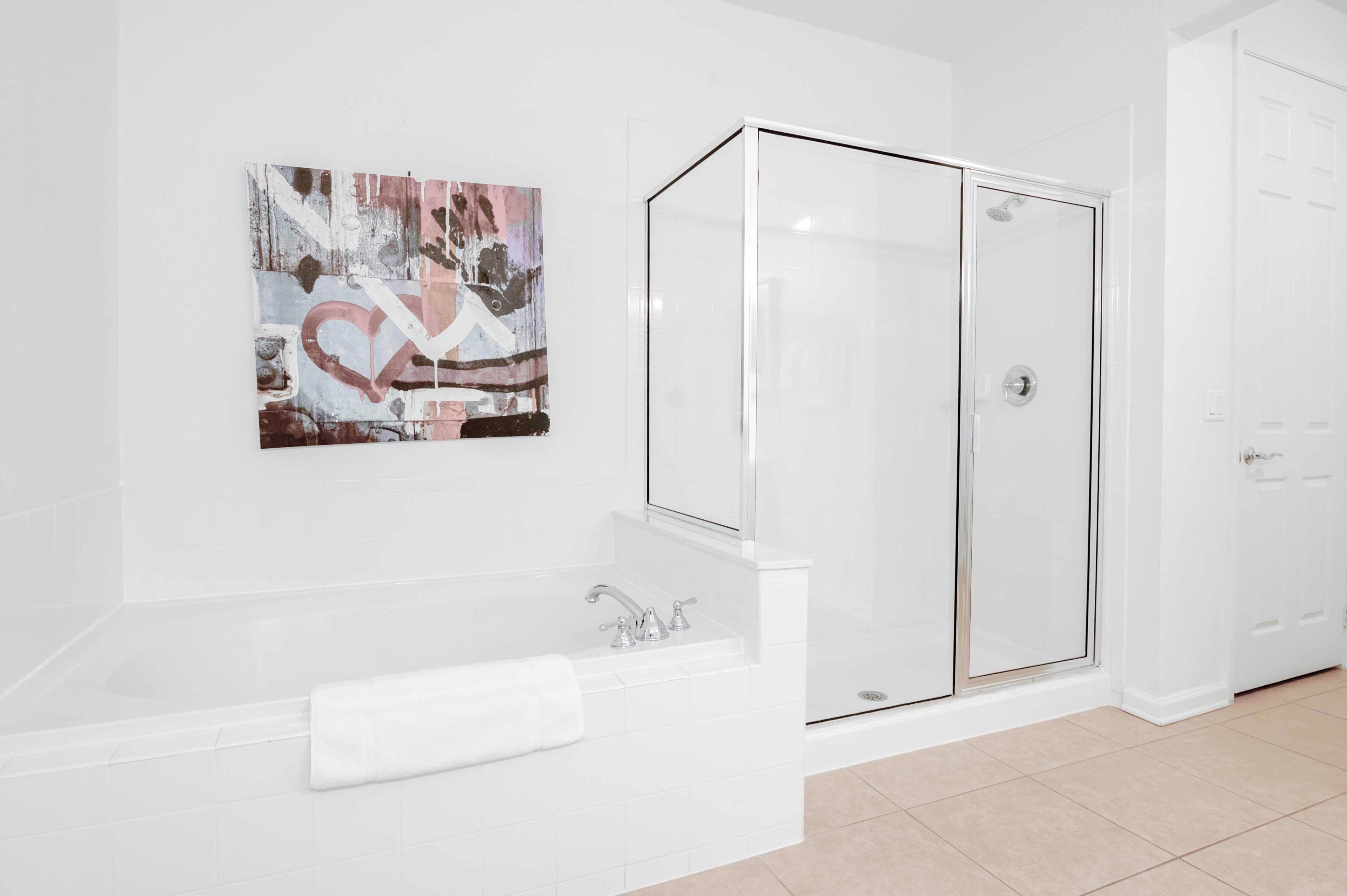 A modern bathroom with a glass-enclosed shower, a white bathtub, and a wall-mounted abstract artwork.