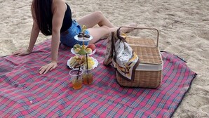Una persona sentada en una toalla de playa con una cesta de picnic y comida.