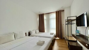 Habitación de hotel con dos camas, televisor, piso de madera y ventana con cortinas.