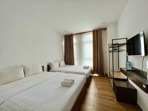 Een hotelkamer met twee bedden, een televisie, een houten vloer en een raam met gordijnen.