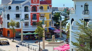 Un edificio colorido con una fuente en primer plano, rodeado de árboles y zonas de estar al aire libre.