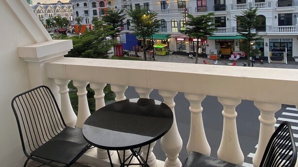 Un balcón con dos sillas negras y una mesa redonda pequeña, con vista a una calle con edificios coloridos y una mezquita.
