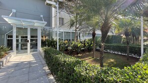 Un bâtiment moderne avec une entrée en verre, entouré d’un espace verdoyant bien entretenu et d’un chemin piétonnier dallé.