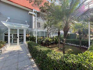 Um edifício moderno com entrada de vidro, cercado por áreas verdes bem cuidadas e um caminho pavimentado.