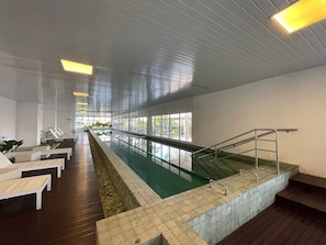A swimming pool with a tiled edge, a wooden deck, and a staircase with metal railings.