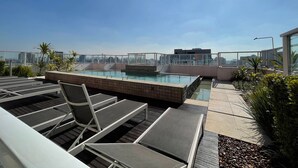Un espace piscine aménagé sur le toit, avec des chaises longues et une vue sur le panorama urbain.