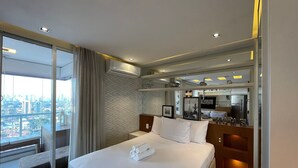 Une chambre d’hôtel avec un grand lit, une vue sur la ville, une cuisine moderne et un grand miroir.