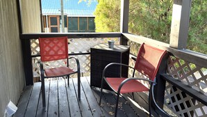 A covered outdoor seating area with two chairs and a small table, overlooking a blue building and trees. - Blue Oasis (Marion)