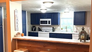 A kitchen with blue cabinets, a white microwave, and a wooden countertop. There are three stools in front of the counter. - Blue Oasis (Marion)