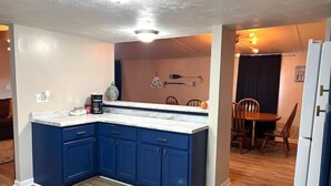 A compact kitchen with blue cabinets, a white countertop, and a wooden dining table in the background. - Blue Oasis (Marion)