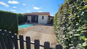 A fenced backyard with a swimming pool, a small building, and a hedge.