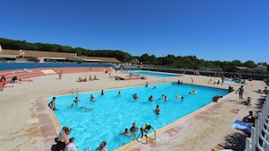 A large outdoor swimming pool with multiple lanes, surrounded by a tiled deck area with sun loungers and umbrellas.