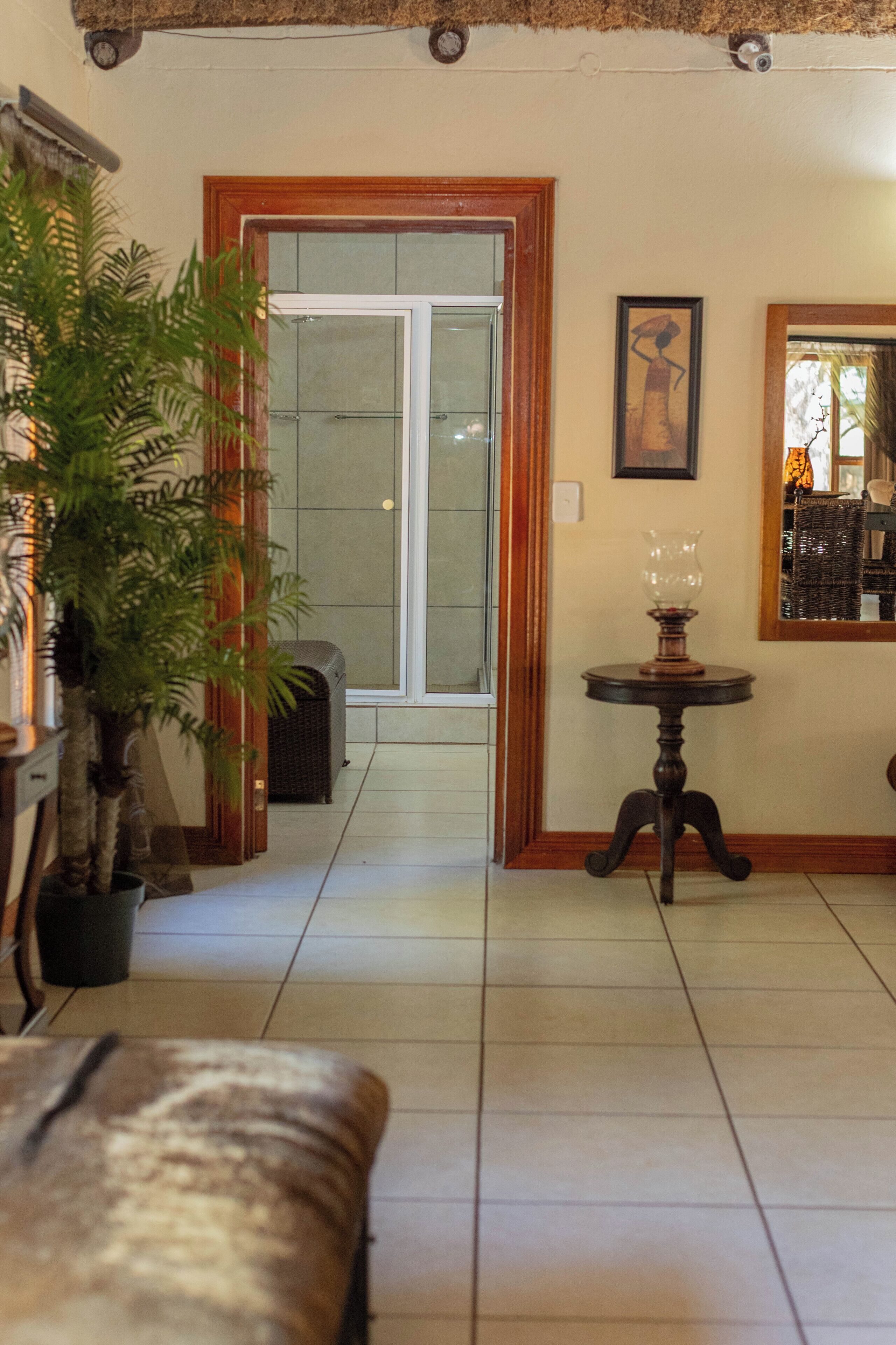 A room with a wooden bench, a potted plant, a table with a lamp, a framed picture, and a sliding glass door leading to a balcony.