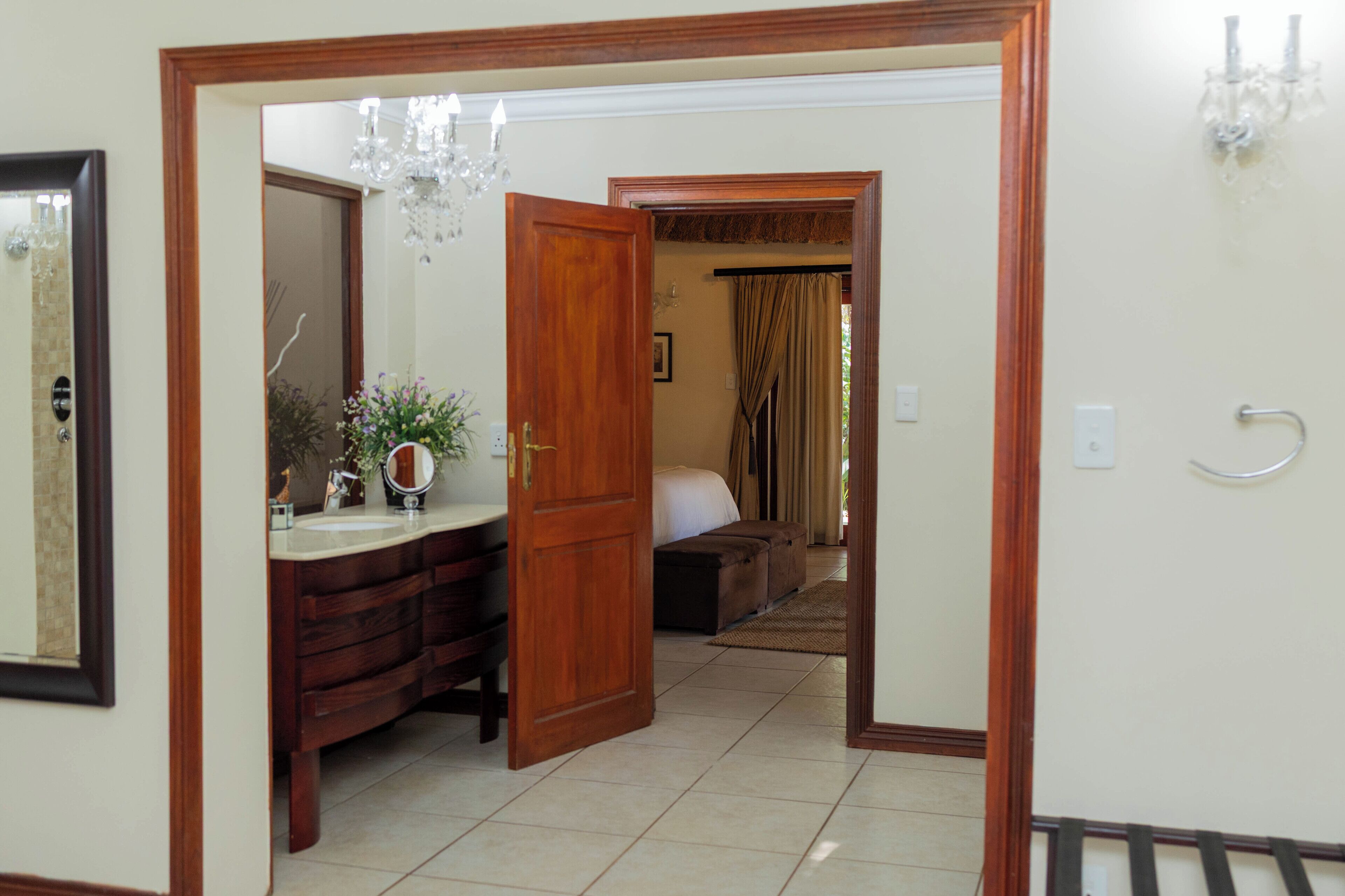 Una habitación de hotel con puerta de madera, baño con espejo, lavamanos y candelabro.