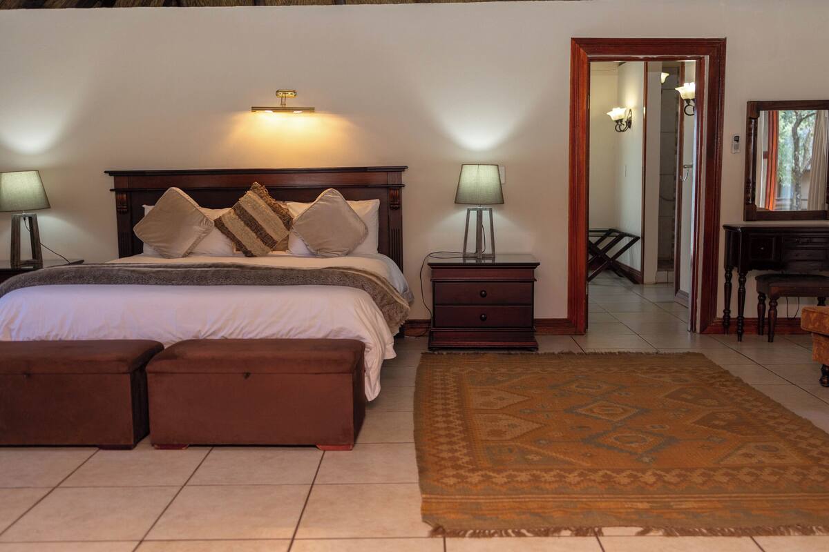 A bedroom with a bed, bedside lamps, a dresser, a mirror, and a patterned rug.