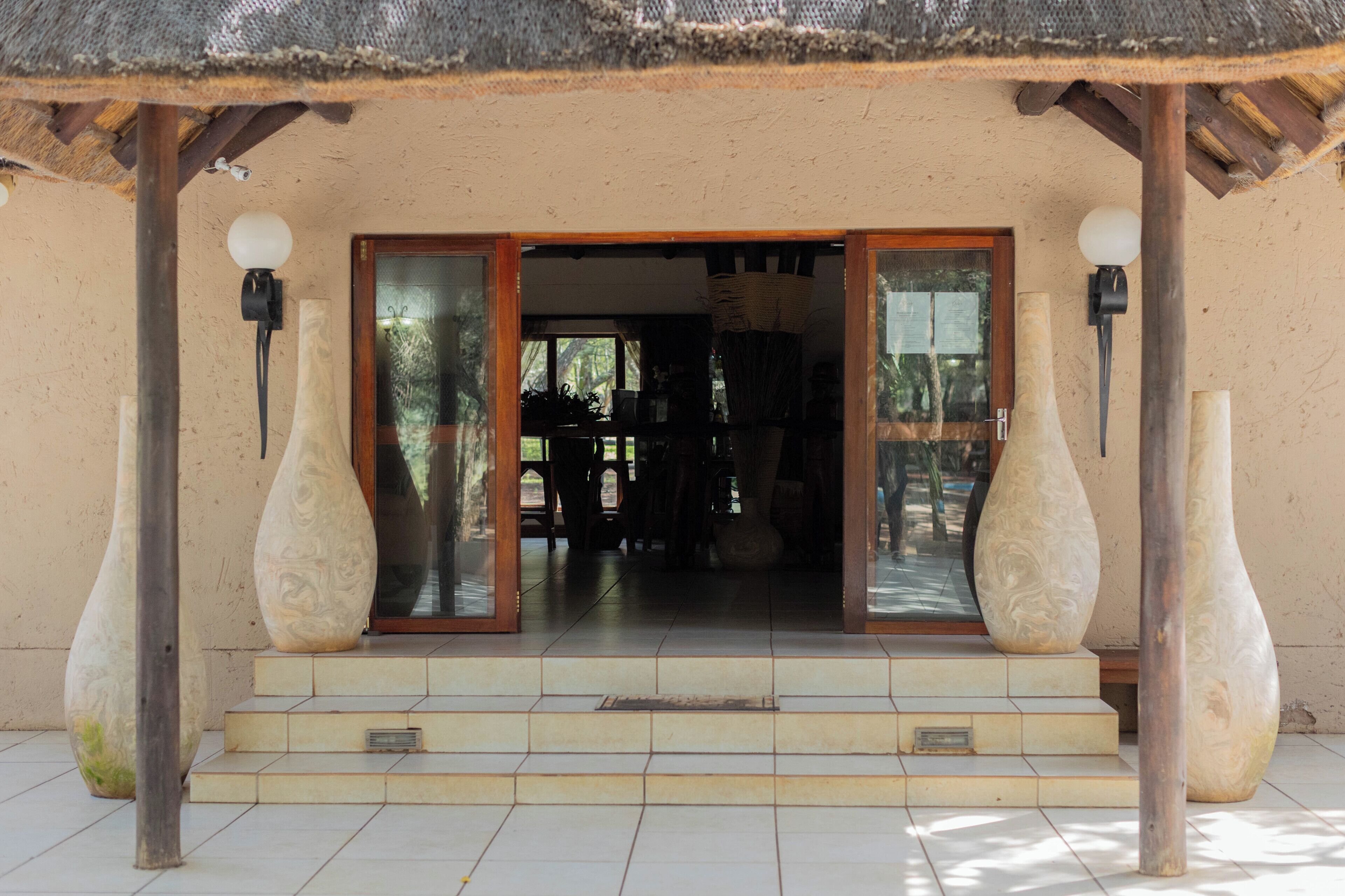 A building entrance with a thatched roof, large vases, and a wooden door.