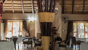 A dining area with tables, chairs, a chandelier, and a thatched roof. - Phakela Private Lodge (Thabazimbi)