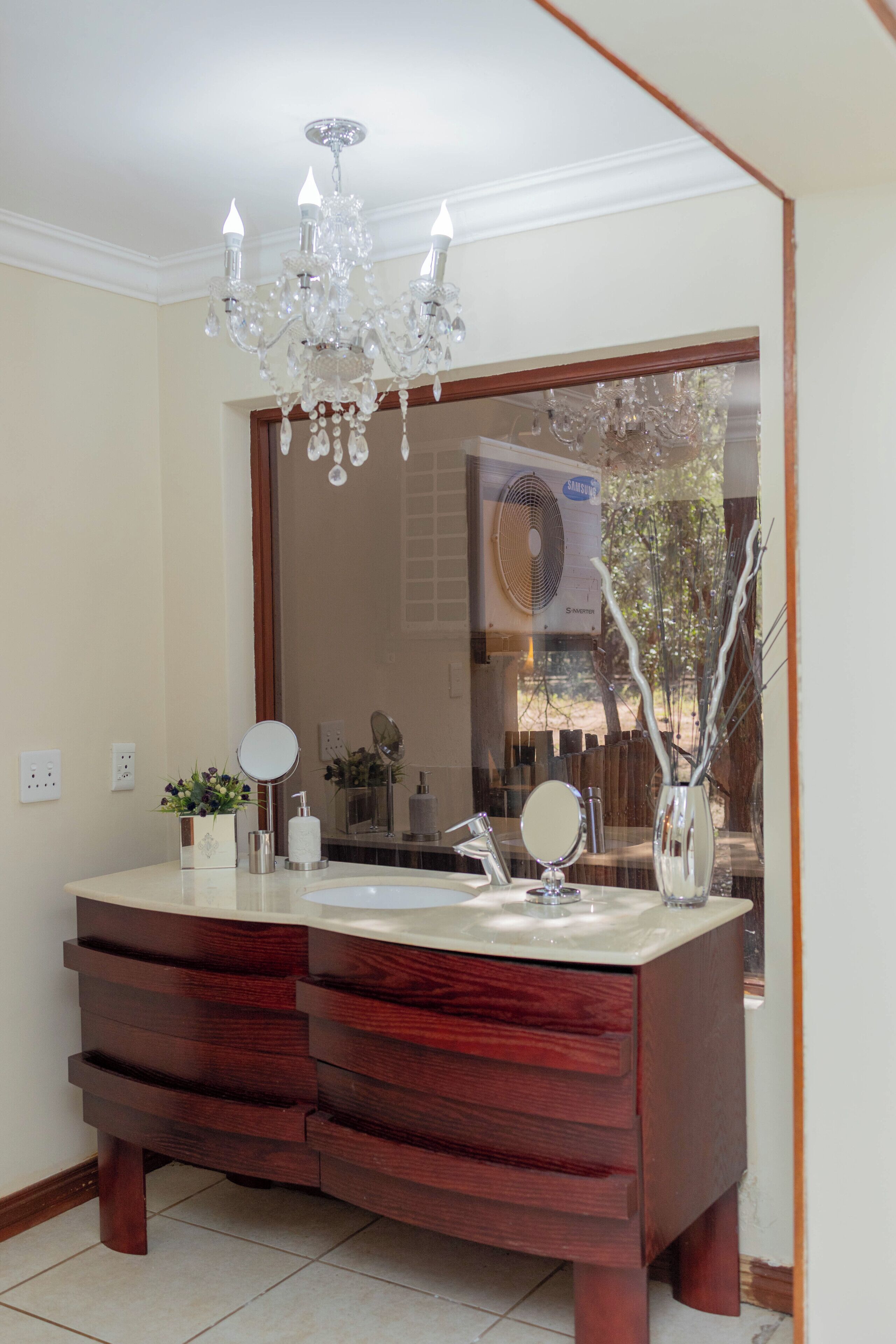 A bathroom with a double vanity, a chandelier, a large mirror, and a view of the outdoors.
